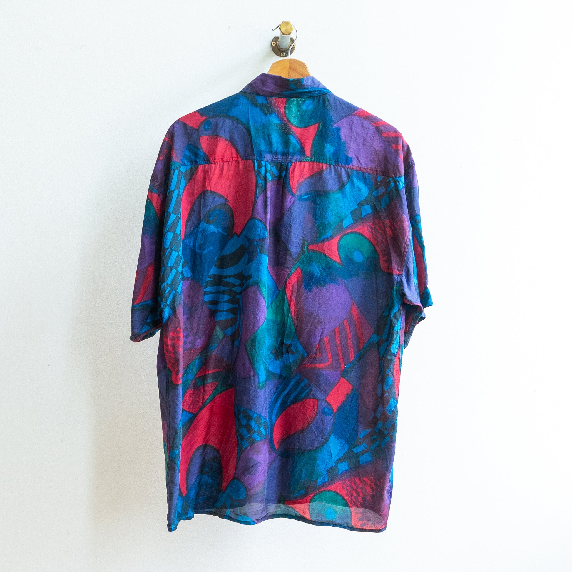 back of a colorful patterned abstract vintage shirt in dark blue purple green red in a soft fabric on a hanger