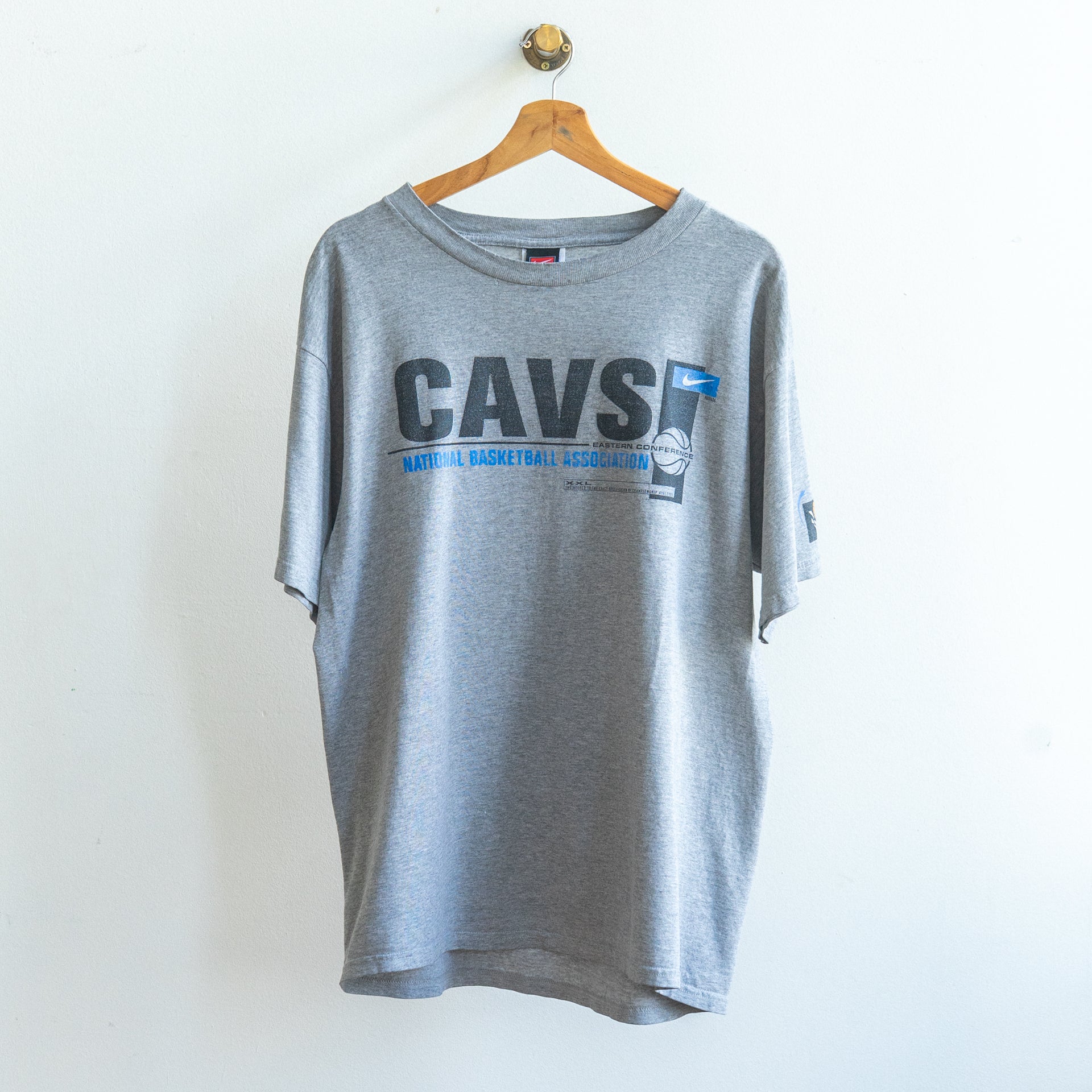 grijze vintage Nike basketbal t-shirt met hoofdletters CAVS in het zwart rechts een kleiner wit nike logo op blauwe achtergrond en blauwe letters national basketball association en een afbeelding van een basketbal ongeveer van de 90s