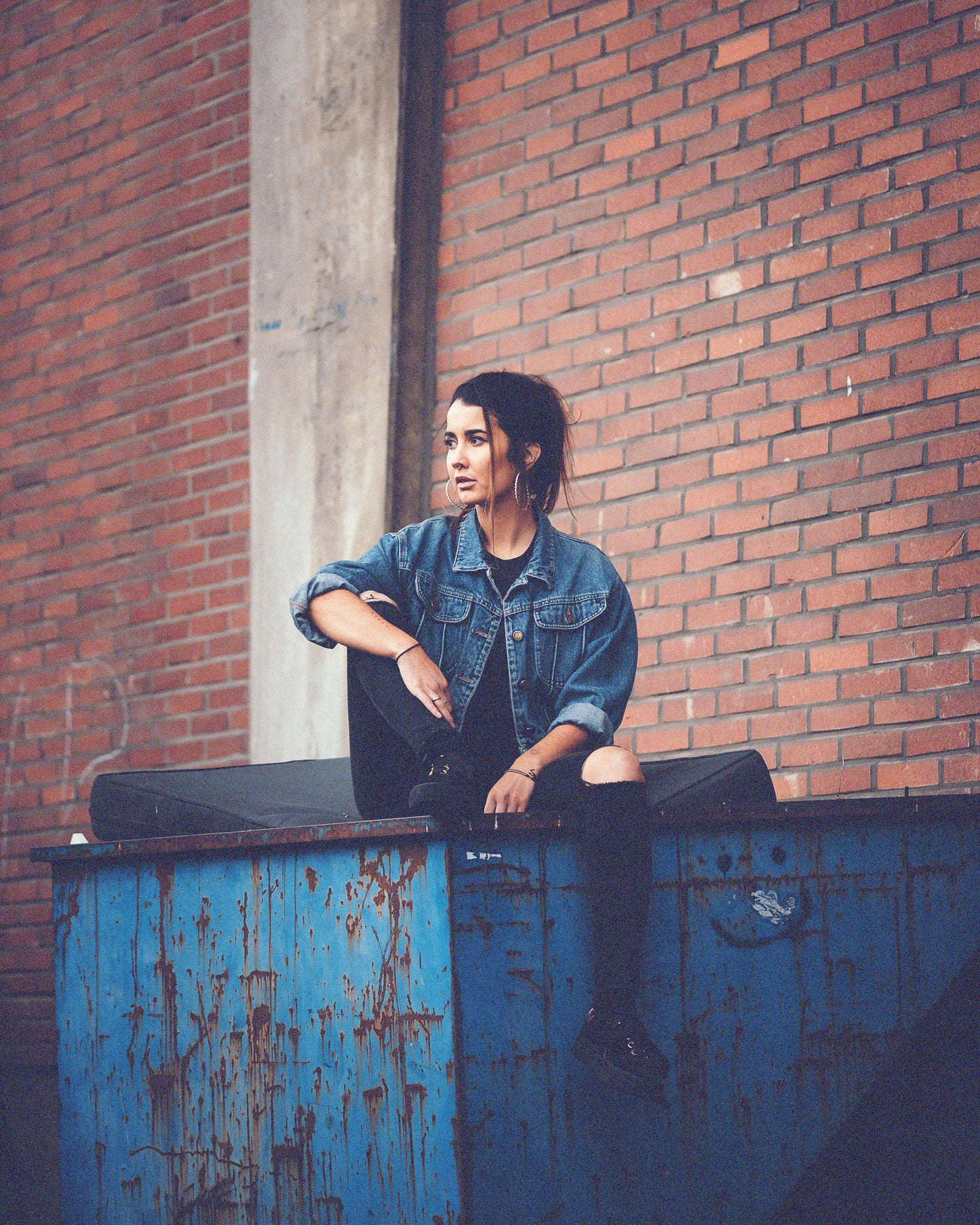 Young-woman-sitting-on-metal-container-wearing-vintage-jeans-jacket-grunge-style